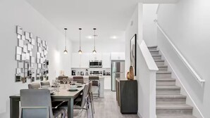 Eine moderne Küche mit Edelstahlgeräten, ein Essbereich mit einem langen Tisch und Stühlen sowie eine Treppe, die zu einer oberen Ebene führt.
