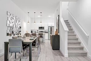 Eine moderne Küche mit Edelstahlgeräten, ein Essbereich mit einem langen Tisch und Stühlen sowie eine Treppe, die zu einer oberen Ebene führt.