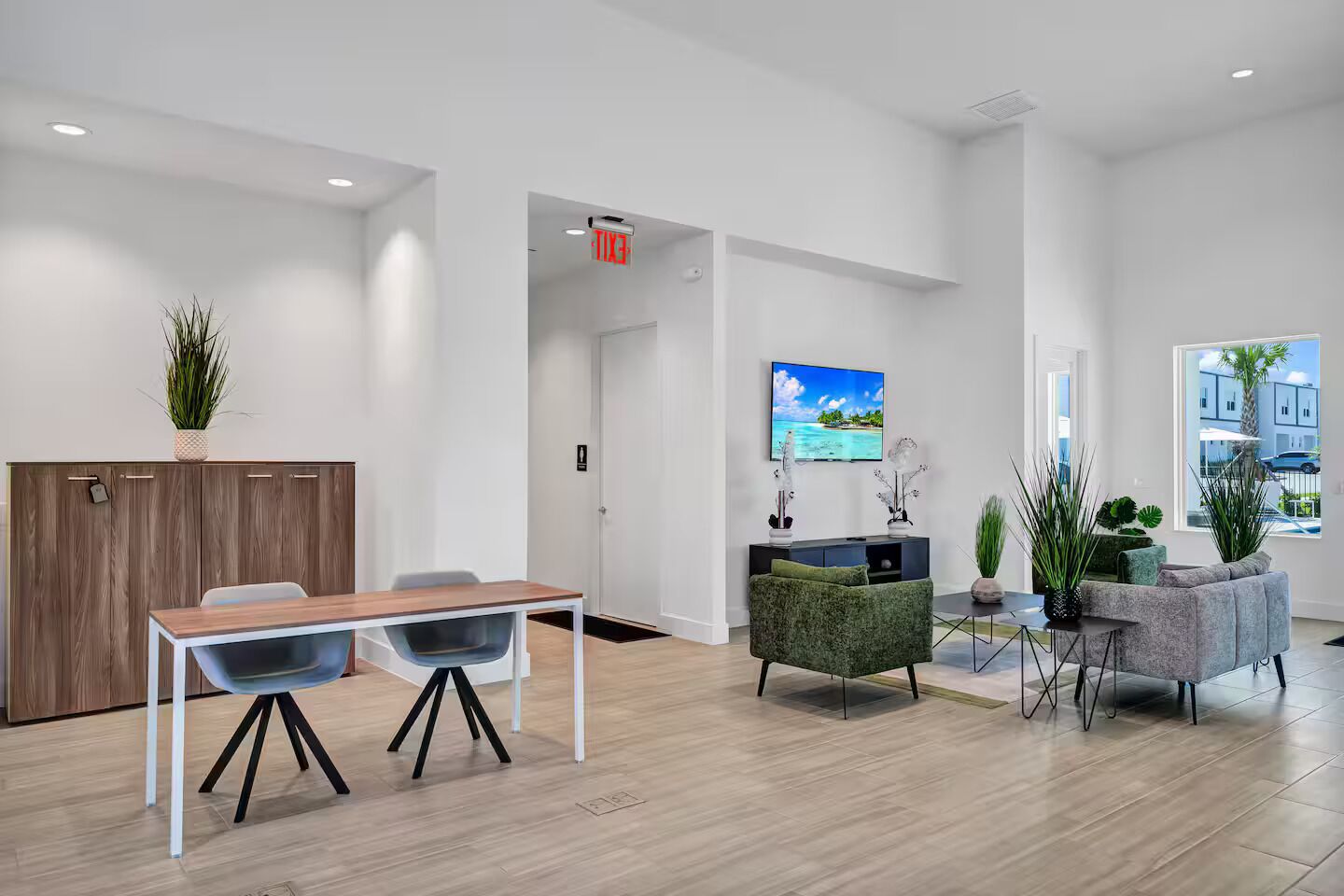 Un espace de bureau moderne avec une table en bois, deux chaises, un canapé vert et un téléviseur fixé au mur.