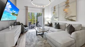 Ein modernes Wohnzimmer mit Flachbildfernseher, Glastisch, einer Couch und abstrakten Wandbildern.