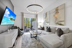 Ein modernes Wohnzimmer mit Flachbildfernseher, Glastisch, einer Couch und abstrakten Wandbildern.