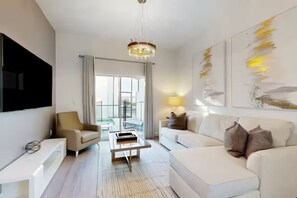 A modern living room with a sofa, armchair, coffee table, and a TV mounted on the wall. - The Sparkling Retreat near Disney w/ private pool (Davenport)