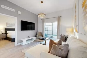 A modern living room with a flat-screen TV, a white sofa, a coffee table, and a chandelier. - The Sparkling Retreat near Disney w/ private pool (Davenport)