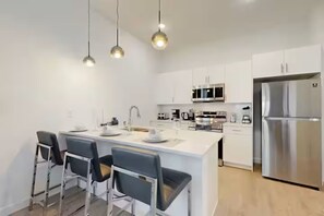 A modern kitchen with white cabinetry, stainless steel appliances, and a central island with bar stools. - The Sparkling Retreat near Disney w/ private pool (Davenport)