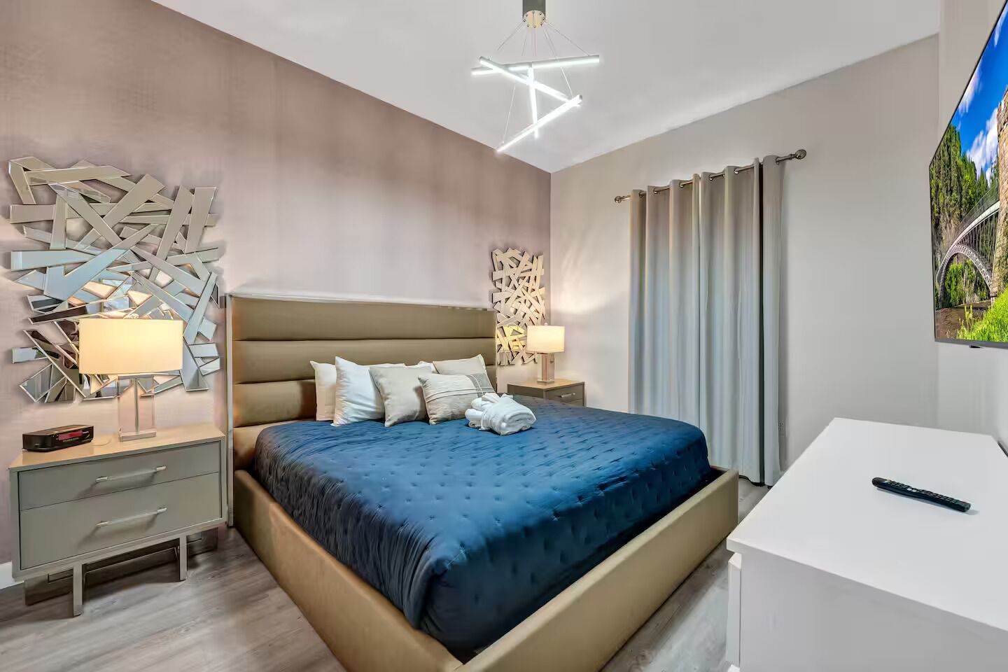 A modern hotel room with a bed, bedside tables, a desk, and a large window with curtains.