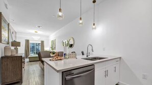 A modern kitchen with a dishwasher, a sink, and a dining area with a table and chairs. - Serendipity @Azur Retreat by Disney w private pool (Davenport)