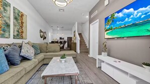 A modern living room with a sofa, coffee table, and a large TV on the wall. - Serendipity @Azur Retreat by Disney w private pool (Davenport)