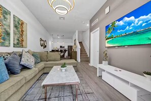 Ein modernes Wohnzimmer mit einer Couch, einem Couchtisch und einem großen Fernseher an der Wand.