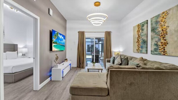 A modern hotel room with a bed, sofa, TV, artwork, and a view through a glass door. - Serendipity @Azur Retreat by Disney w private pool (Davenport)