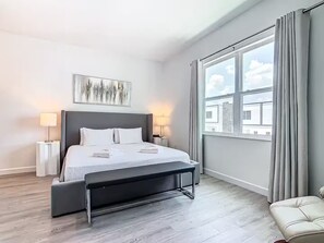Et moderne hotelværelse med en stor seng, sengeborde med lamper, udsigt til bygninger gennem vinduet og en grå gulv.