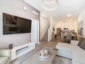 Ein modernes Wohnzimmer mit Flachbildfernseher, einer Couch, einem Couchtisch und einer Treppe, die zur Küche führt.