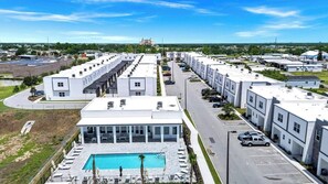 Et moderne hotel med pool, flere parkeringspladser og udsigt over det omkringliggende område.