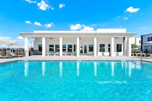 Ein modernes Hotel mit Schwimmbad, überdachter Außenbestuhlung und blauem Himmel.