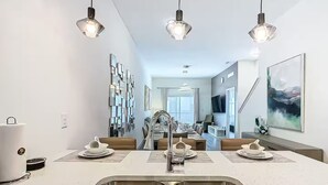 Una cucina moderna con un lavello doppio, un'area pranzo con tavolo apparecchiato per quattro persone e illuminazione a sospensione.