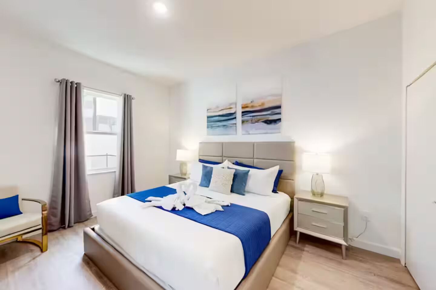 Une chambre d’hôtel moderne avec un grand lit, une table de chevet, une chaise et une fenêtre avec des rideaux.