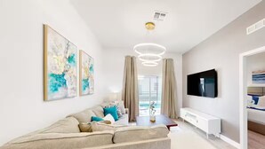 Una sala de estar moderna con un sofá, televisor, arte abstracto y vistas al exterior.
