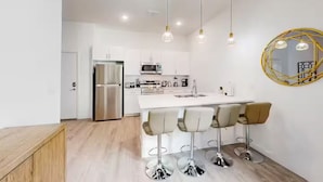 Una cocina moderna con una isla central, taburetes de bar, lámparas colgantes y un elemento decorativo en la pared.