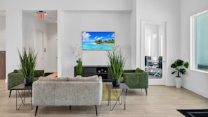 Una sala de estar moderna con un sofá, dos sillones verdes, una mesa de centro, un televisor montado en la pared y plantas en macetas.