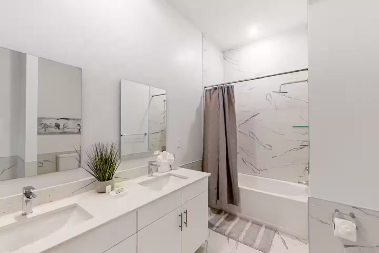 A modern bathroom with a large mirror, two sinks, a shower, and a potted plant.