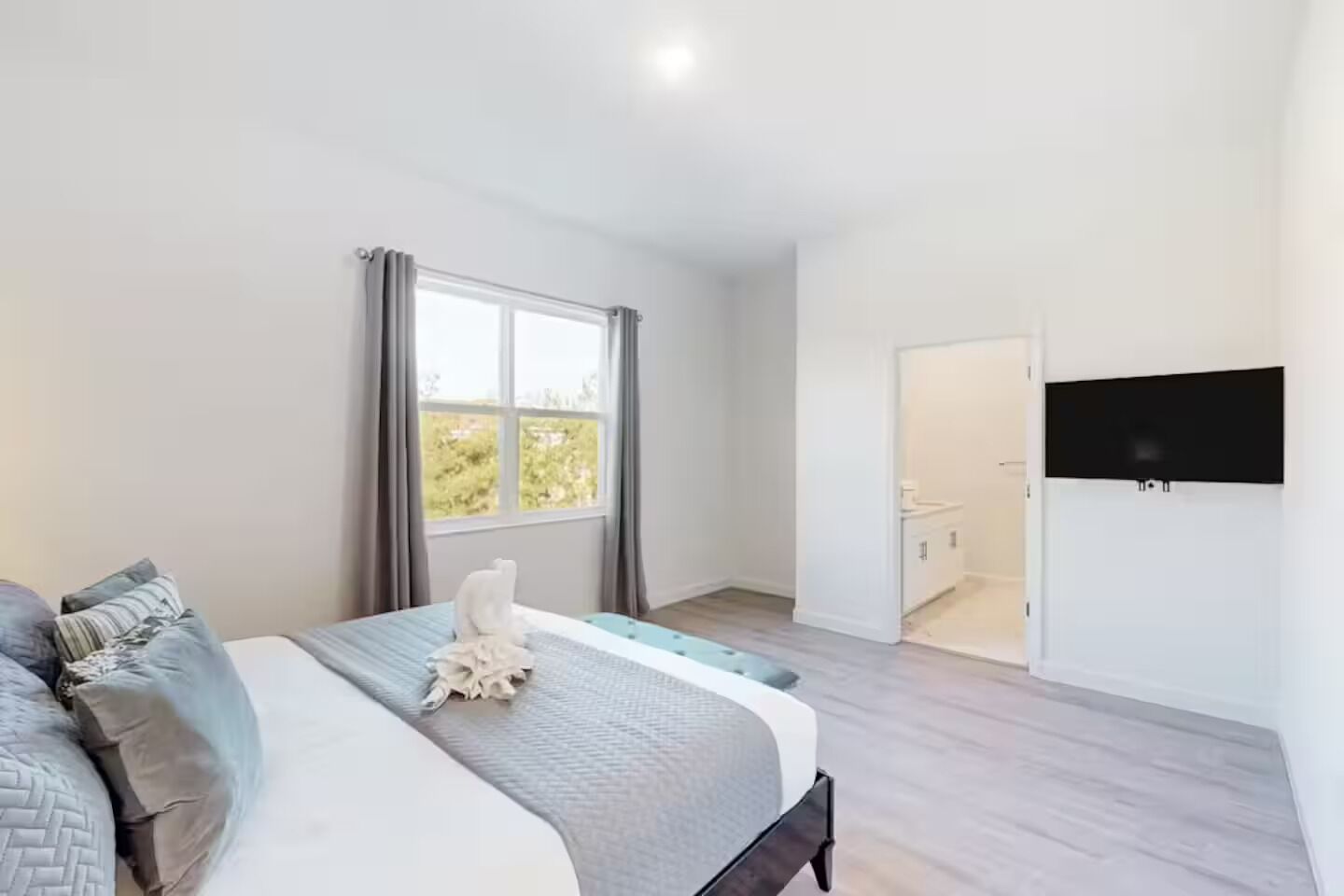 Een slaapkamer met een bed, een raam, een aan de muur bevestigde televisie en een deur naar een badkamer.