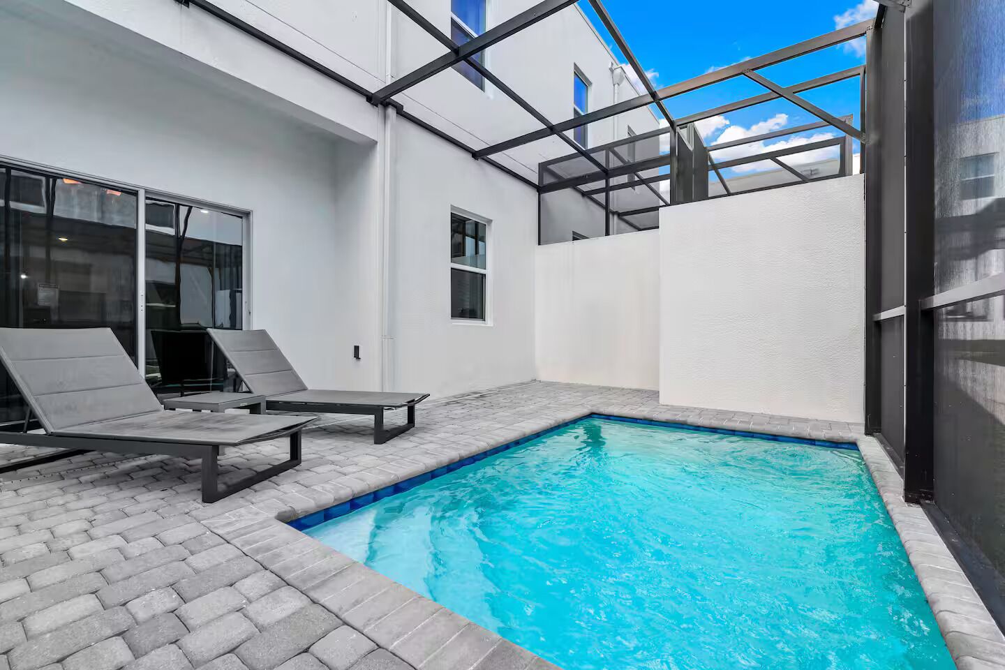 Ein Pool mit zwei Liegestühlen, einer Pflasterterrasse und einem Gebäude mit großen Fenstern.