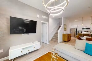 A modern living room with a flat-screen TV, white entertainment unit, and a staircase leading to a kitchen. - The Onyx Retreat by Disney / Universal/ Seaworld (Davenport)