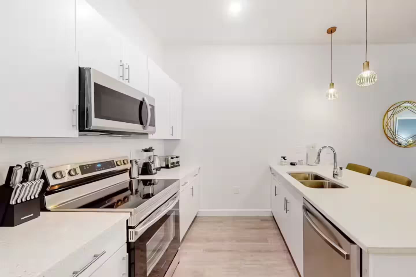 Una cocina moderna con armarios blancos, microondas, horno, cafetera y lavamanos.