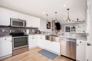 Une cuisine moderne avec des armoires blanches, des appareils en acier inoxydable et des luminaires suspendus.