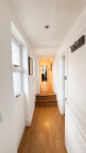 Un couloir étroit avec un plancher en bois, des murs blancs et une porte sur le côté droit.