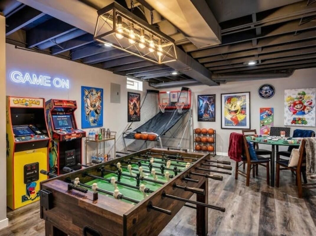 Ein Raum mit einem Kicker, Spielautomaten und einem Neonlichtschild mit der Aufschrift 'GAME ON'.