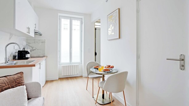 Uma cozinha moderna com bancada de mármore, área de refeições com mesa redonda e cadeiras, e uma janela grande que proporciona luz natural.