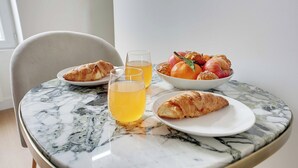 Uma mesa com croissants, uma tigela de frutas e um copo de suco de laranja.