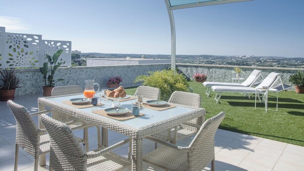 Une terrasse sur le toit, avec une table dressée pour deux personnes, entourée de chaises en osier, offrant une vue sur le paysage urbain.