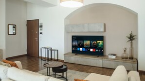 Un salon moderne avec un téléviseur à écran plat fixé au mur, un canapé, une table basse et une petite table d’appoint.