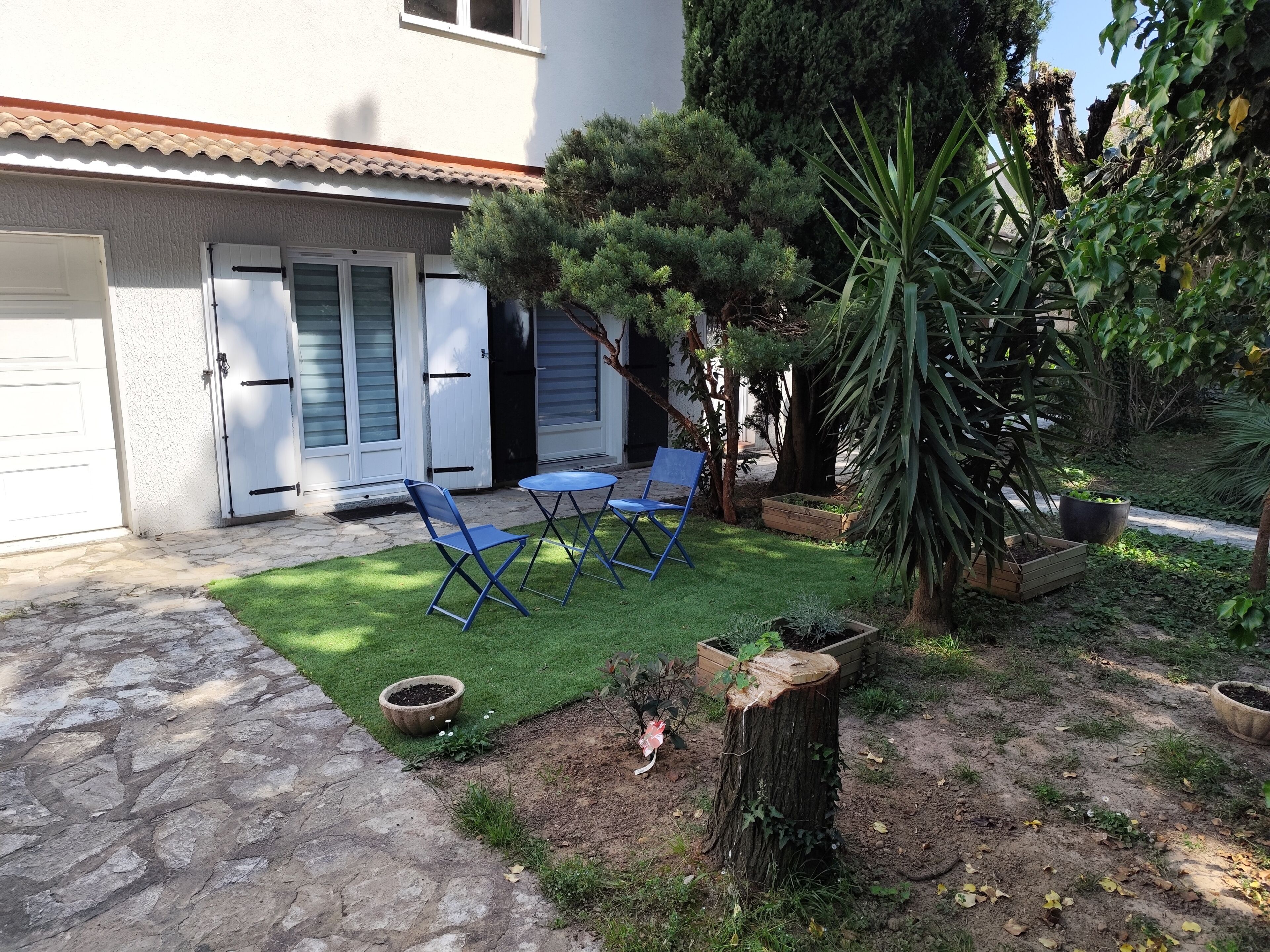 A patio with a lawn, a wooden bench, and a tree.