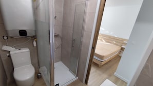 A bathroom with a toilet, a shower enclosure, and a bed.