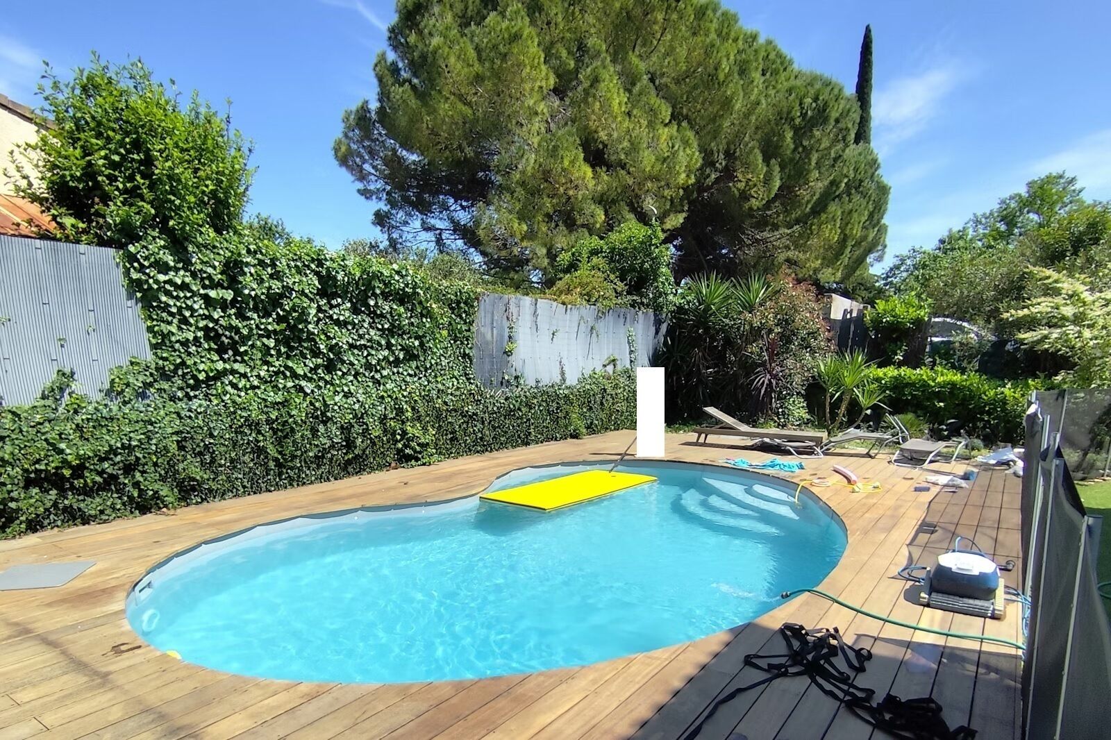 Piscina com deck de madeira, um tapete flutuante amarelo e cadeiras de descanso.