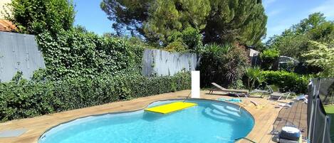 Piscina com deck de madeira, um tapete flutuante amarelo e cadeiras de descanso.