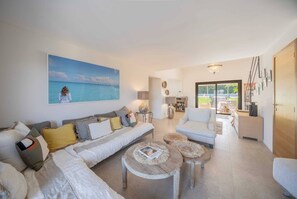 Ein modernes Wohnzimmer mit einem großen Gemälde vom Strand, einer Couch, einem Couchtisch und einem Essbereich mit Aussicht.
