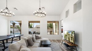 Ein modernes Wohnzimmer mit einer Eckcouch, einem Esstisch, einem Fernseher und großen Fenstern.