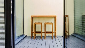 Una mesa de madera y dos taburetes en un balcón con vistas a un edificio.