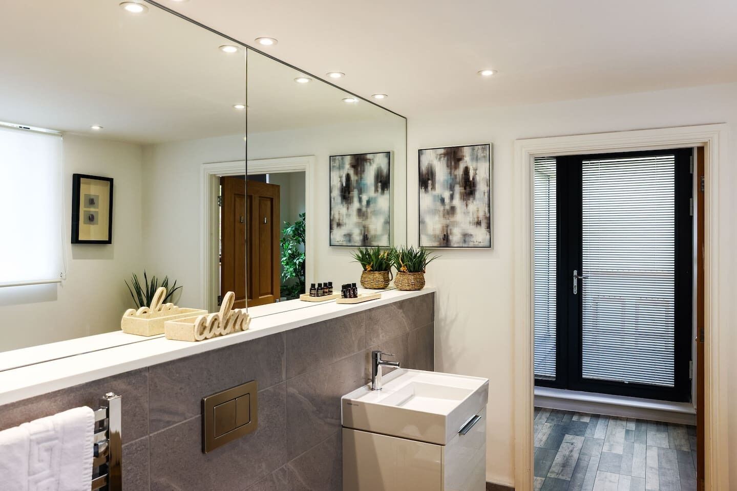 A modern bathroom with a large mirror, a vanity with a sink, and a window with blinds.
