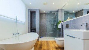 Un baño moderno con una bañera independiente, ducha con mampara de vidrio y tocador blanco.