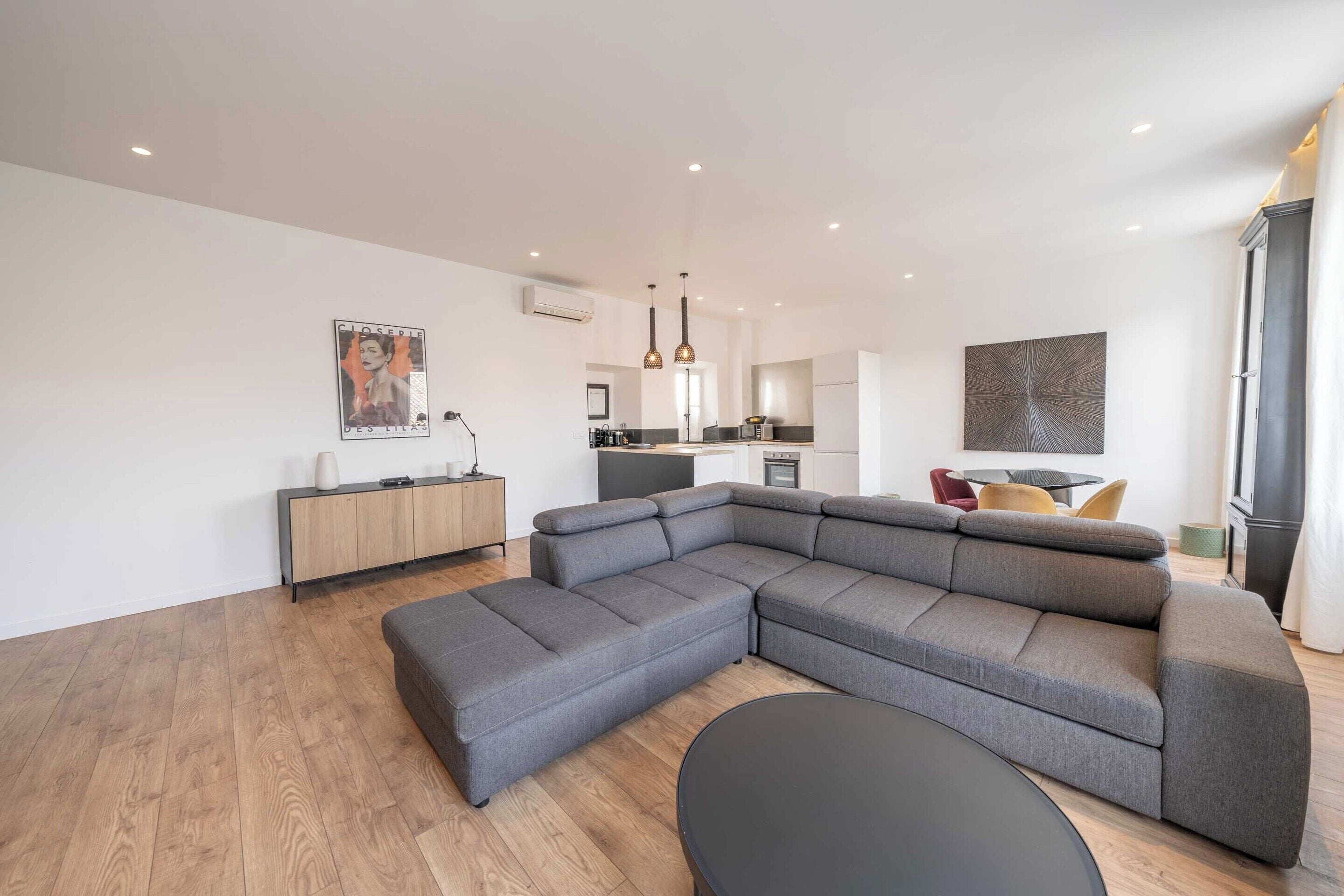 Un salon moderne avec un canapé d’angle, un coin repas et une cuisine en arrière-plan.