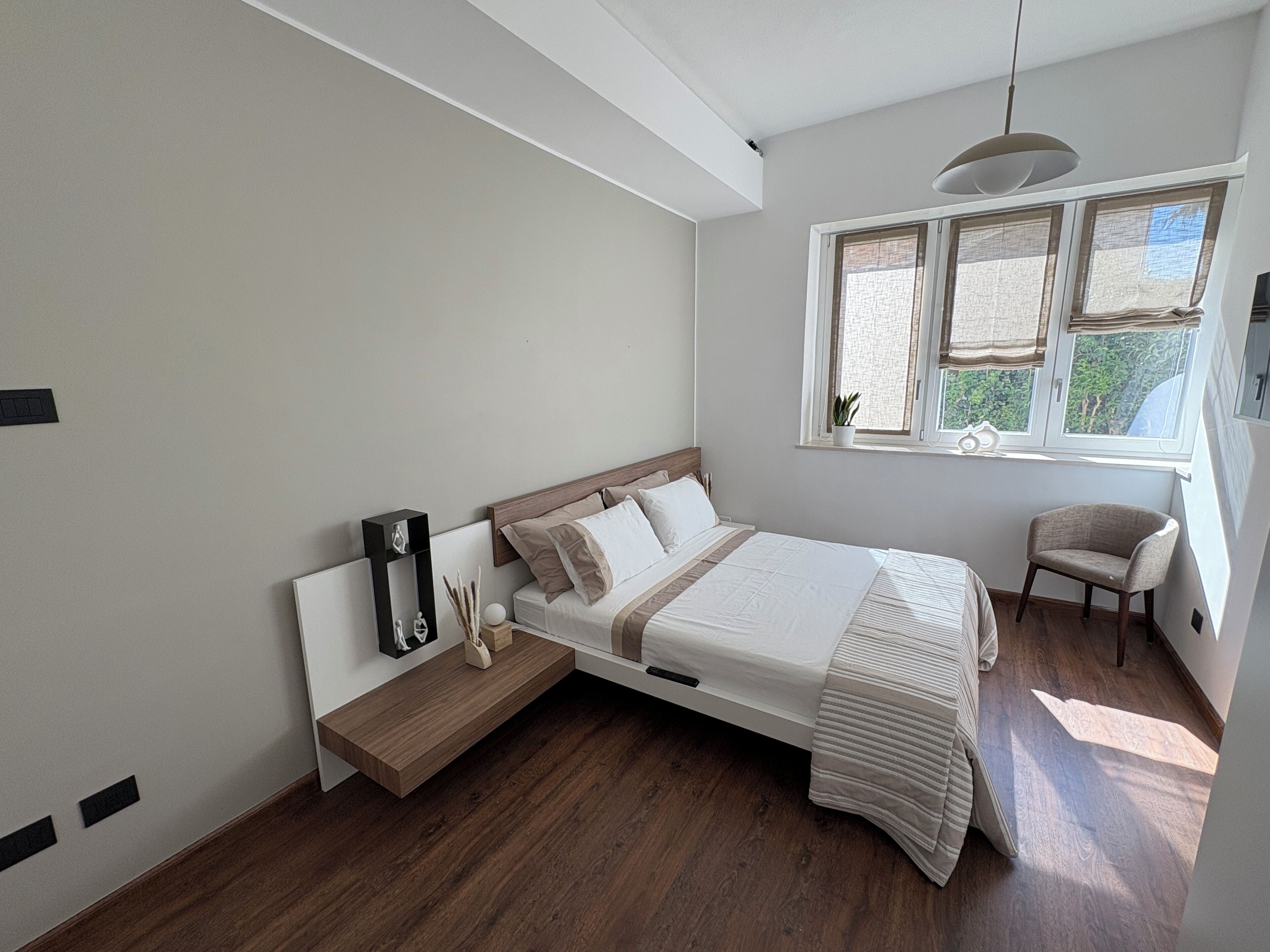 Une chambre à coucher comprenant un lit, une table de chevet, une chaise, une fenêtre et un plancher en bois.