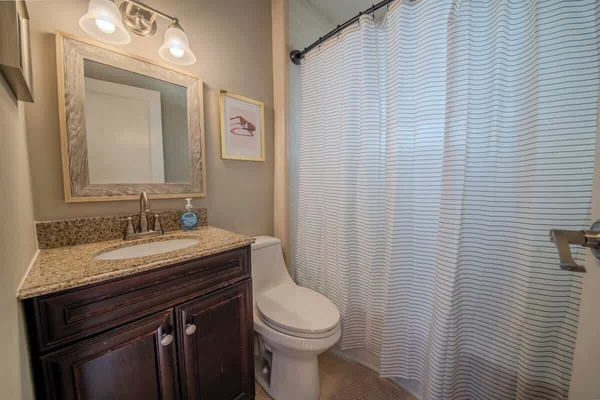 Baño con lavamanos, espejo, inodoro y cortina de ducha a rayas.