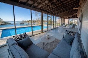Un espace extérieur abrité, aménagé avec des sièges, et offrant une vue sur une piscine et un lac.