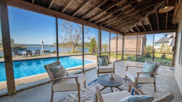 A covered outdoor area with a pool, wicker furniture, and large windows offering a view of the outdoors. - The Bungalow, Pool, Dock, Kayaks, & Game Room (Topping)