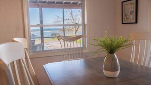 A dining area with a table, chairs, a window with a view of the outdoors, and a framed picture on the wall. - The Bungalow, Pool, Dock, Kayaks, & Game Room (Topping)
