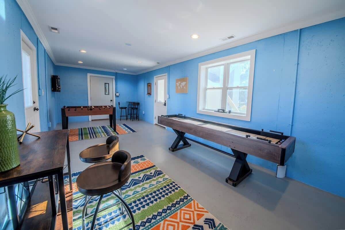 A room with blue walls, a foosball table, a pool table, and a bar area with stools.